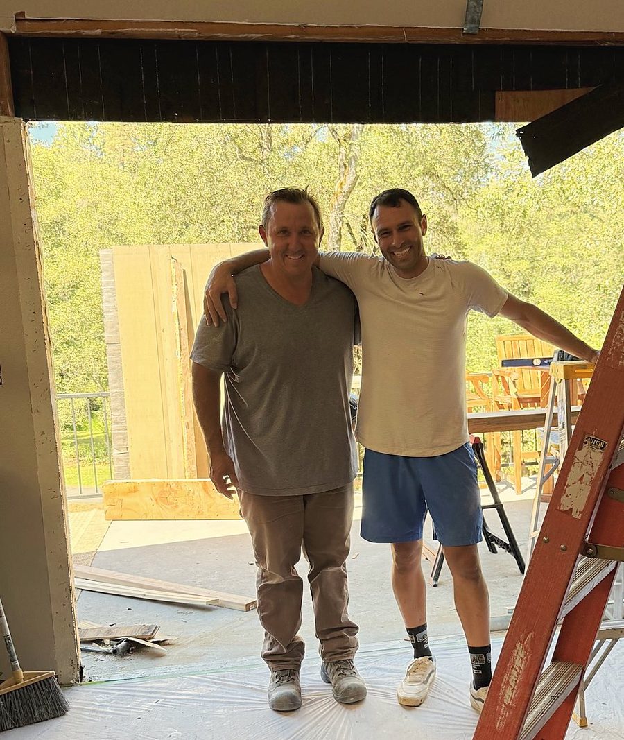 Daniel and Russ with arms around each other in the opened-up wall of Daniel’s house during the remodel